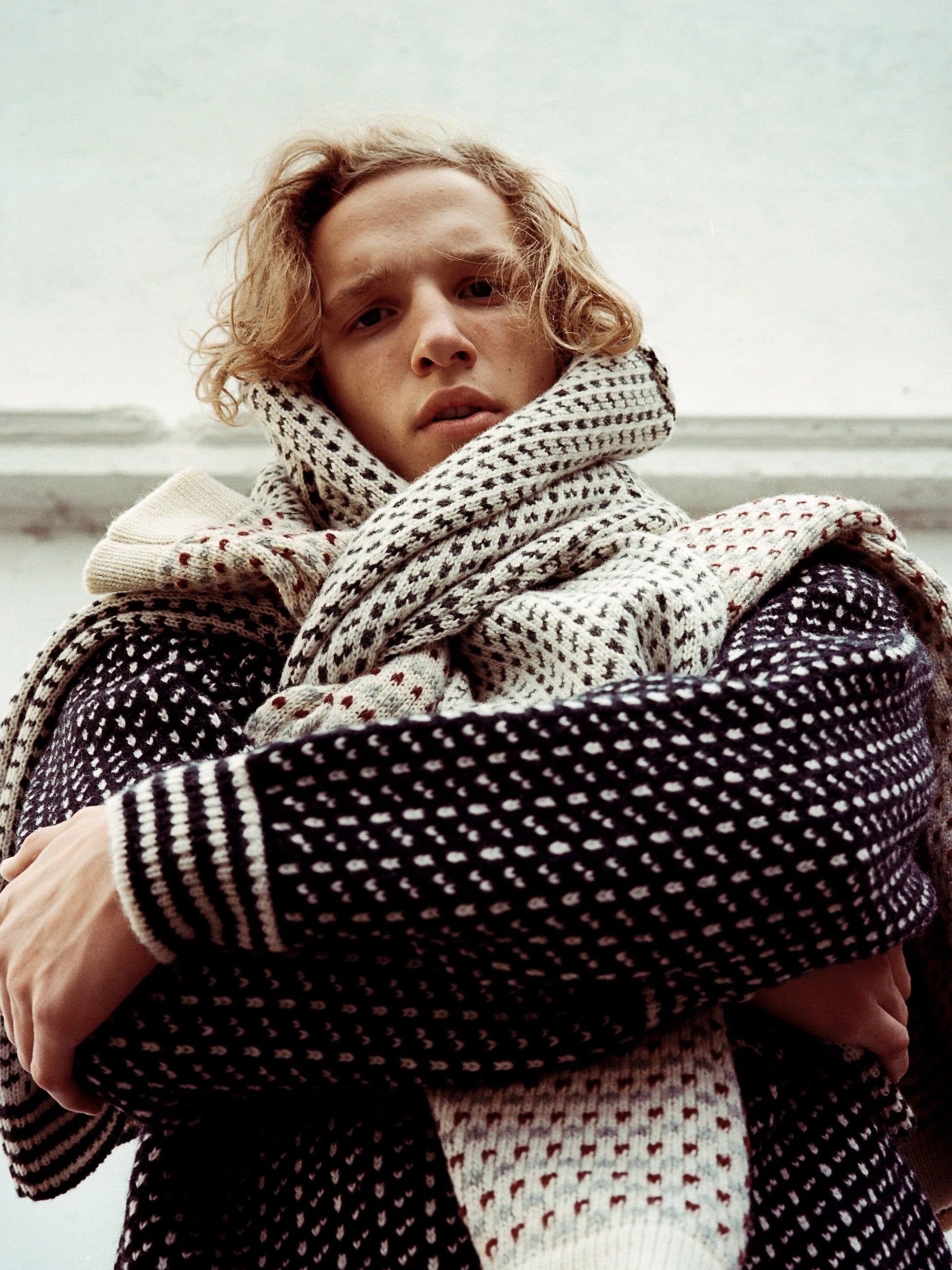 Primer plano de una persona con prendas de punto en capas alrededor del cuello y los hombros, con patrones y texturas intrincados de Norlender Knitwear - Knitwear.