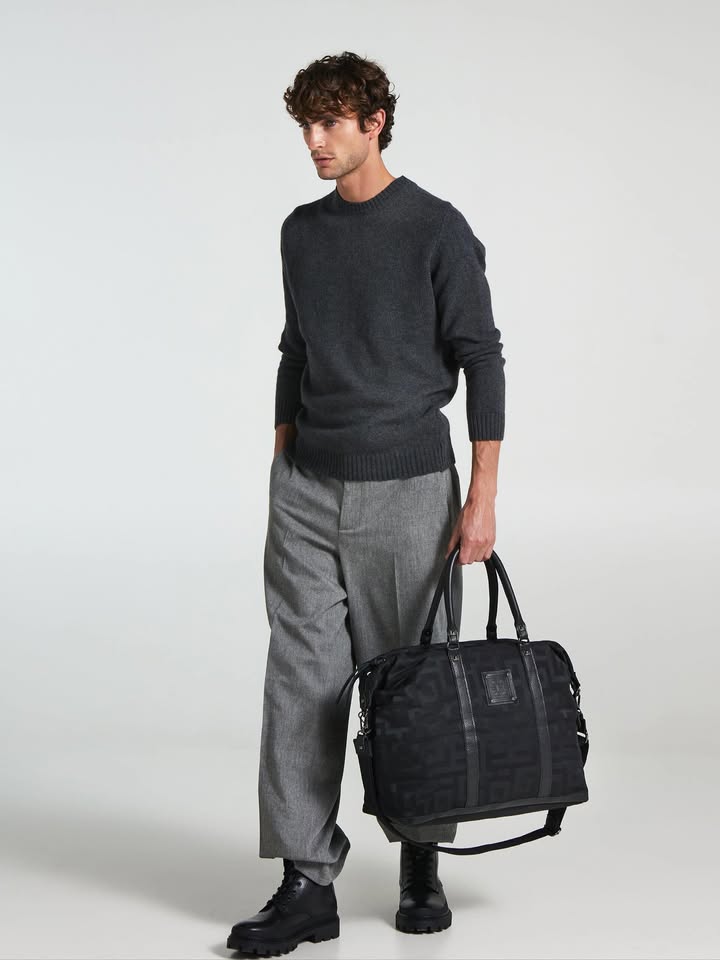 alt
Un homme vêtu d’un pull gris foncé et d’un pantalon gris clair tenant un sac de voyage noir avec poignées et bandoulière, mettant en valeur le sac Ames.