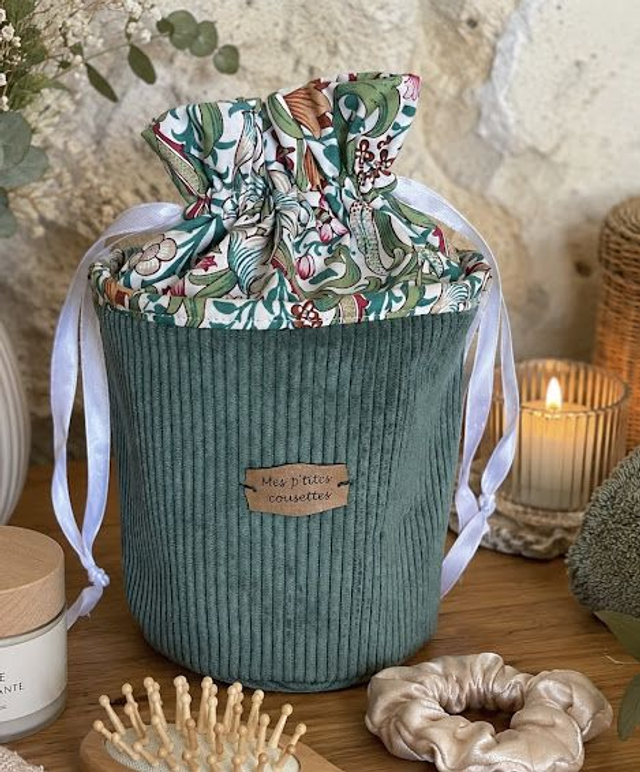 Green textured basket with floral fabric lid on a wooden surface with decorative items.