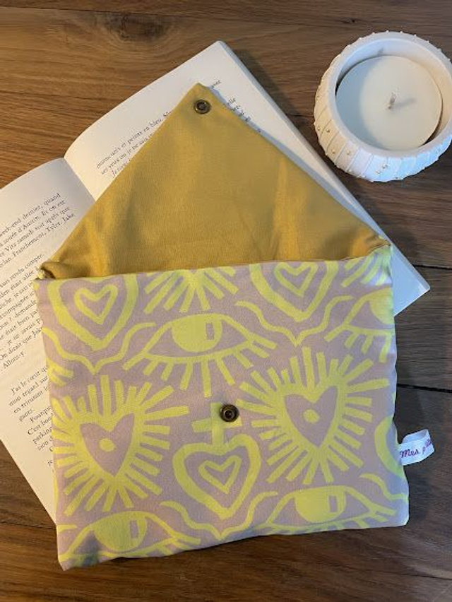 Fabric pouch with heart and eye pattern on a wooden surface with an open book and candle.